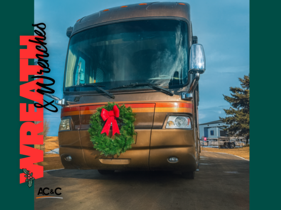 A brown motorhome parked outdoors with a green holiday wreath displayed on the front grille, decorated for Christmas.