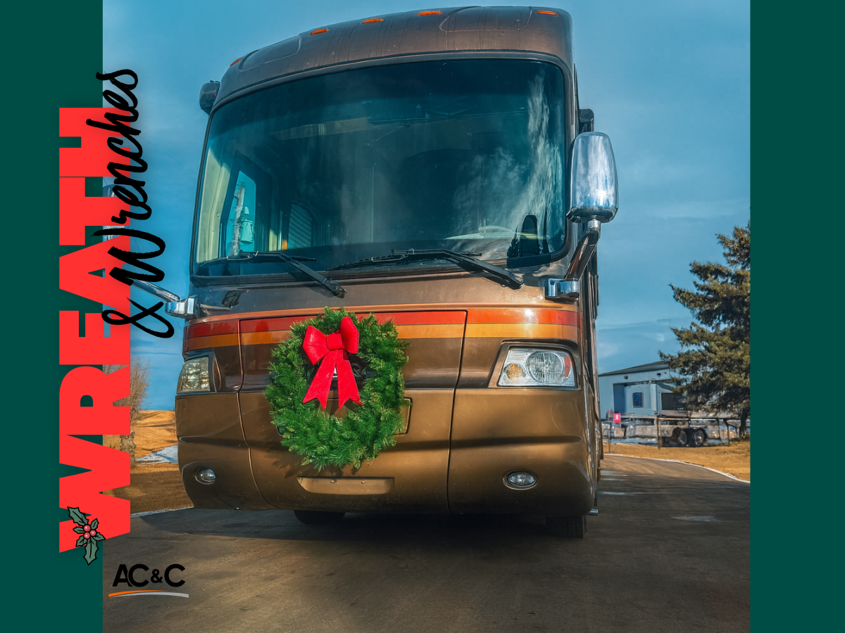 A brown motorhome parked outdoors with a green holiday wreath displayed on the front grille, decorated for Christmas.
