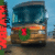 A brown motorhome parked outdoors with a green holiday wreath displayed on the front grille, decorated for Christmas.