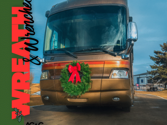 A brown motorhome parked outdoors with a green holiday wreath displayed on the front grille, decorated for Christmas.