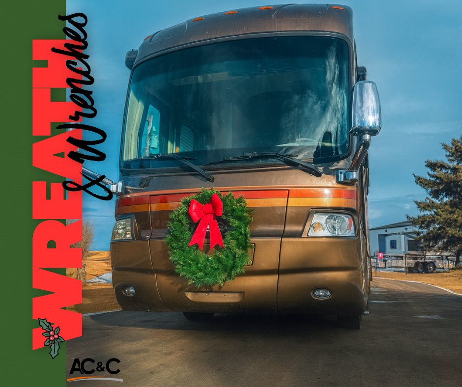 A brown motorhome parked outdoors with a green holiday wreath displayed on the front grille, decorated for Christmas.